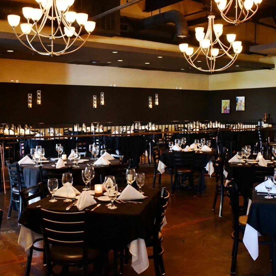 Elegant restaurant dining room with black tablecloths, set tables, chandeliers, and a bar area.