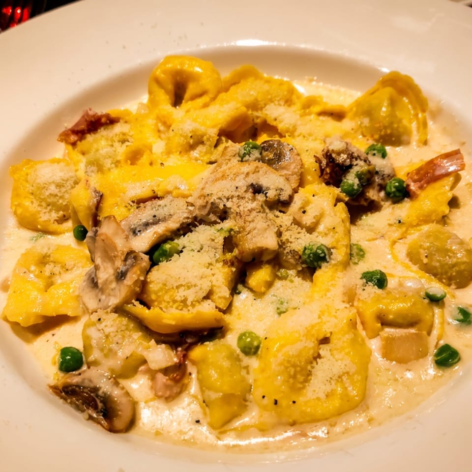 Tortellini pasta in a creamy sauce with mushrooms, peas, and bacon, topped with Parmesan cheese.