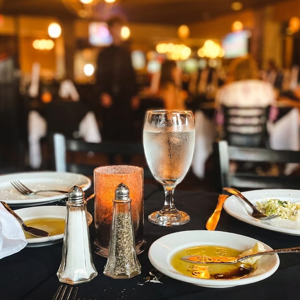 A restaurant table set with bread, olive oil, and partially eaten dishes, with blurred diners in the background.