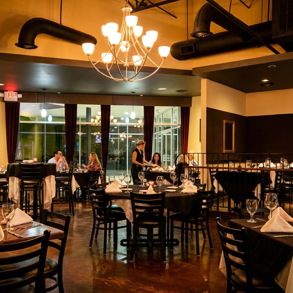 A dimly lit restaurant interior with set tables, patrons dining, and a server attending to guests.