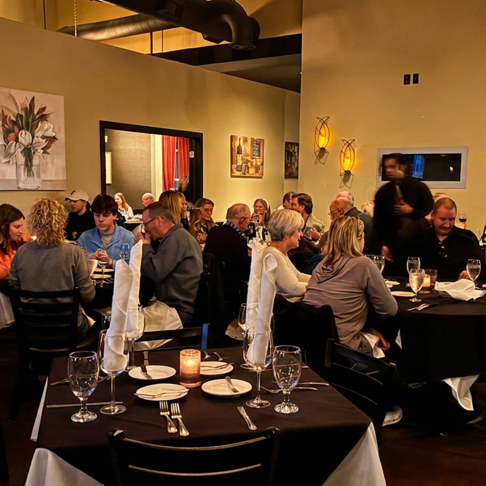 A dimly lit restaurant dining room filled with patrons seated at tables with black tablecloths.