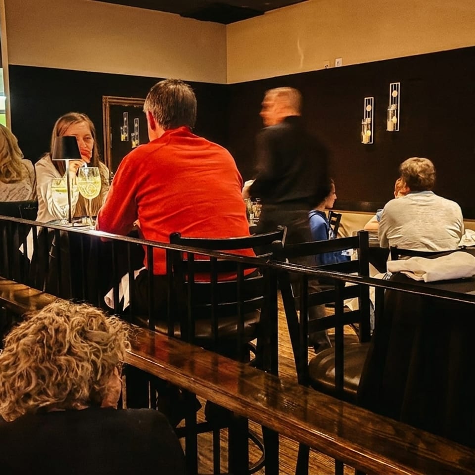 Diners enjoying meals and drinks in a dimly lit, upscale restaurant with dark tables and walls.